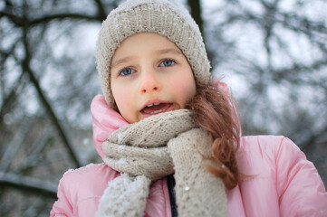 Sad child girl in warm knitted winter clothes spent time outdoors and got frozen.