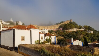 Fototapeta na wymiar Obidos, Portugal : Cityscape of the town with medieval houses, wall and the Albarra tower. Obidos is a medieval town still inside castle walls, and very popular among tourists