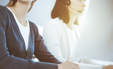 Obraz premium Call center. Group of operators at work. Focus on beautiful woman receptionist in headset at customer service office. Business concept