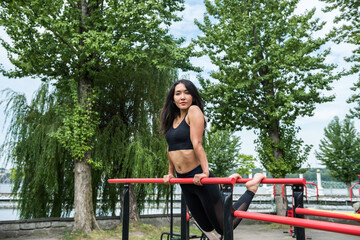 Naklejka premium Beautiful sexy woman makes exercise on horizontal bar sunny day for perfect street workout