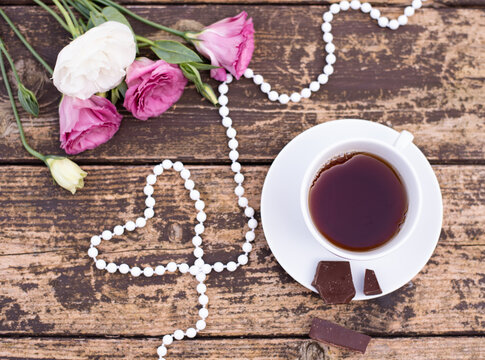 Morning time, beautiful picture for blog post in Instagram. Relax and have cup of coffee or tea with dark chocolate, decorate by flowers and beads as heart, enjoy your free minutes. Wooden background