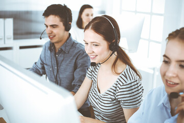 Casual dressed young woman using headset and computer while talking with customers online. Group of operators at work. Call center, business concept