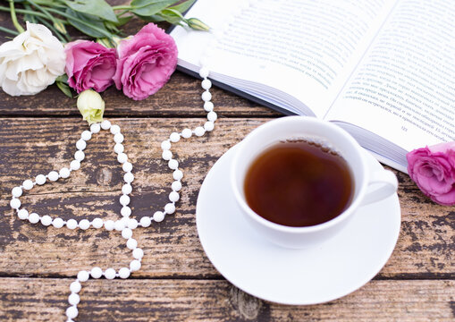 Morning time, beautiful picture for blog post in Instagram. Relax and have cup of coffee or tea with book, decorated by flowers and beads as heart. Enjoy your free minutes. Wooden background