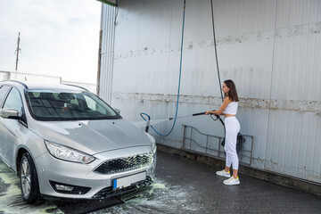 Happy cute woman cleans her car with high-pressure water gun