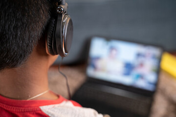 Shoulder shot teenager kid with headphone listening online class - concept of online virtual education, new normal and homeschooling due to coronavirus covid-19 pandemic.