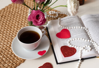 Magic mood atmosphere of love picture for post in Instagram. Take break, rest with coffee and book, decorated by hearts and beads, with flowers in glass vase on table. Learning is development. Layout.