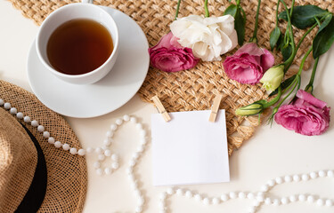 Obraz na płótnie Canvas Unusual, beautiful composition for post on Instagram. Cup of tea, flowers, beads, piece of paper on clothespins and hat on brown napkin background. Free minute at work and enjoyment from rest. Closeup