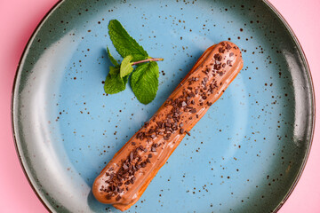 Tasty eclair with chocolate filling over pink background. French cuisine concept, dessert for tea...