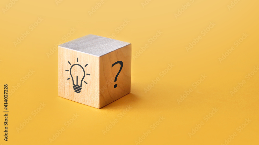 Poster a wooden cube with a picture of a question on one side and a burning light bulb on the other.