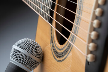 microphone leaning on the body of an acoustic guitar with gray background