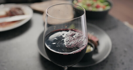 closeup pour red wine in wineglass with steak on background