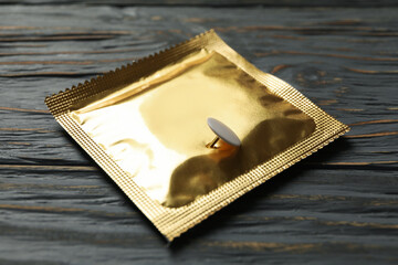 Condom with pin on wooden background, close up