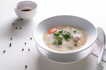 Pork Congee original food thai in white cup with sauce in cup on white table. contain of eggs, rice, spring onions, coriander, ground Pork. asian breakfast in the morning and baby food concept.