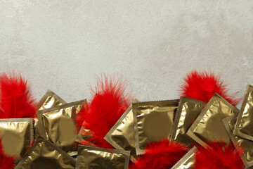 Frame of condoms with feathers on white textured background, space for text