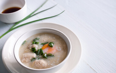 Pork Congee original food thai in white cup with sauce in cup on white table. contain of eggs, rice, spring onions, coriander, ground Pork. asian breakfast in the morning and baby food concept.