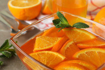 Fototapeta na wymiar Concept of dessert with bowl of orange jelly with orange slices on gray table, close up