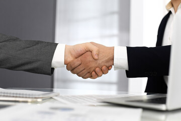 Unknown diverse business people are shaking hands finishing up meeting at the desk in office, close-up. Handshake concept