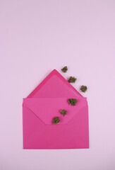 Cannabis dry herb going out of pink post letter, on a pink background. Sending cannabis wishes. Minimal concept. Monochromatic women day.  