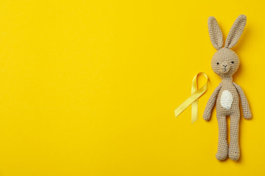Toy bunny and child cancer awareness ribbon on yellow background