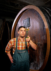 Obraz na płótnie Canvas Viticulteur dans une cave avec des cuves en bois qui goûte son vin en Alsace