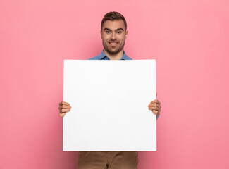 happy young guy in denim shirt presenting empty white board