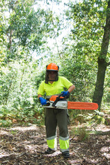 female forestry worker or lumberjack using chainsaw to cut trees in forest
