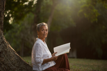 Asian elderly woman reading a book under a tree in the park