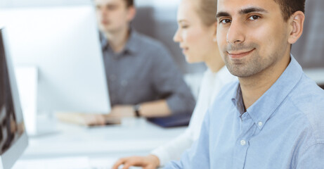 Obraz premium Business people working together in modern office. Happy smiling adult businessman using pc computer with colleagues. Teamwork and partnership concept