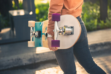 Close up hands of woman holding skateboard or surf skate in park at morning. Healthy lifestyle concept.