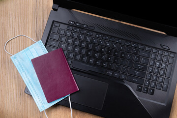 Wooden table background with laptop , near a medical protective mask and a passport. New normal...
