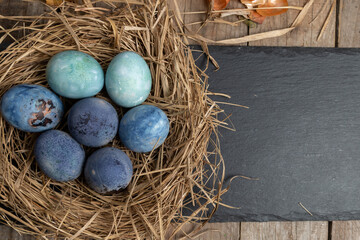 Easter background with Easter eggs in a nest on a wooden table. Top view with copy space. 