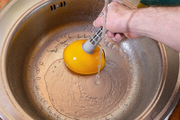 A plunger in a man's hand cleans a clogged sink, close-up.