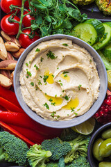 Traditional hummus in gray bowl with vegan snacks. Plant based diet concept.
