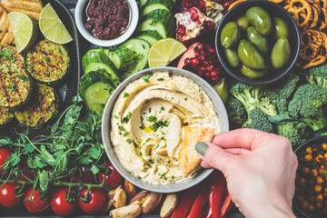 Vegan charcuterie board. Hummus bowl with vegetables, fried chickpeas, olives, falafel and pita bread. Plant based diet concept.