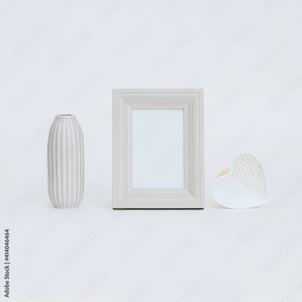 Poster closeup view of a white picture frame with a long vase and a heart-shaped object on white