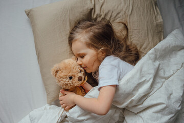 Little girl sleeping in bed embracing soft toy at home, top view