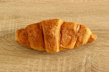 Freshly baked viennoiserie croissant isolated on wooden table. Closeup, soft focus at the background