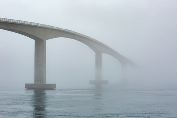 Bridge over fjord fading into fog on a dull day in Norway