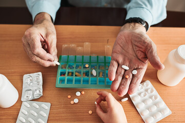 Senior man organizing his medication into pill dispenser. Senior man taking pills from box. Healthcare and old age concept with medicines. Medicaments on table - 414048050