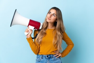 Young hispanic woman over isolated blue background holding a megaphone and thinking