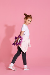 adorable little child girl with skateboard over pink background. side view.