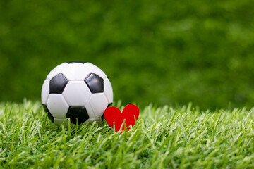Soccer ball with love red heart are on green grass