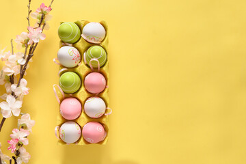 Easter pastel eggs in yellow carton box and spring blooming flowers on yellow. View from above. Space for text.