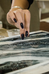 a girl with a black manicure pours a hard transparent crumb on an epoxy painting