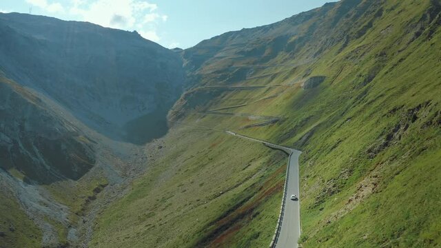 Reveling aerial shot of white car driving on Stelvio Pass with a hairpin corners on a sunny day. Highest paved mountain road in the Eastern Alps.