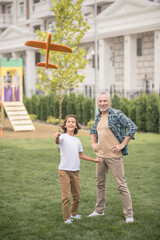 Cute dark-haired boy playing woth a toy plane together with his dad and feeling happy