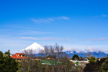 Snow covered cone of Mount Taranaki is clearly visible behind city suburb. New Zealand