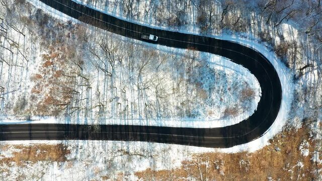 Snowy winter serpentines forest with little traffic on the road on the hill.