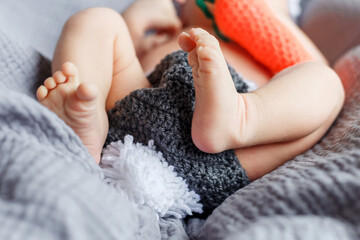 Close up of newborn baby's feet. Baby's tiny little toes on the gray blanket. Even skin color. Small feet of a child. Child's feet. Baby feet close up. Knitted bunny costume for a newborn photo shoot.