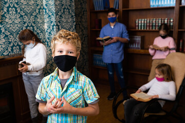 Fototapeta premium Pensive tween boy in protective mask solving puzzles in escape room with friends. New norms in pandemic, precaution for viral infections